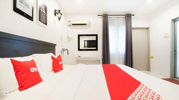 A hotel room with a large bed, red and white bedding, a mounted TV, and a window with curtains.