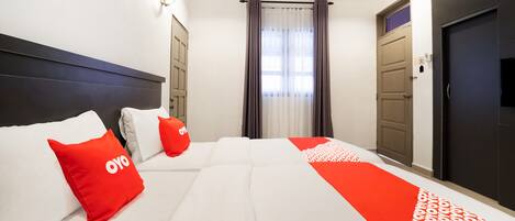 A hotel room with a large bed, two pillows, a red blanket, and a window with curtains.