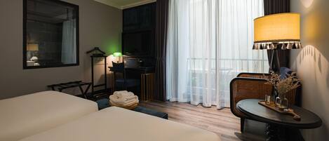 Habitación de hotel con dos camas, un escritorio con silla, una lámpara y vistas al exterior.