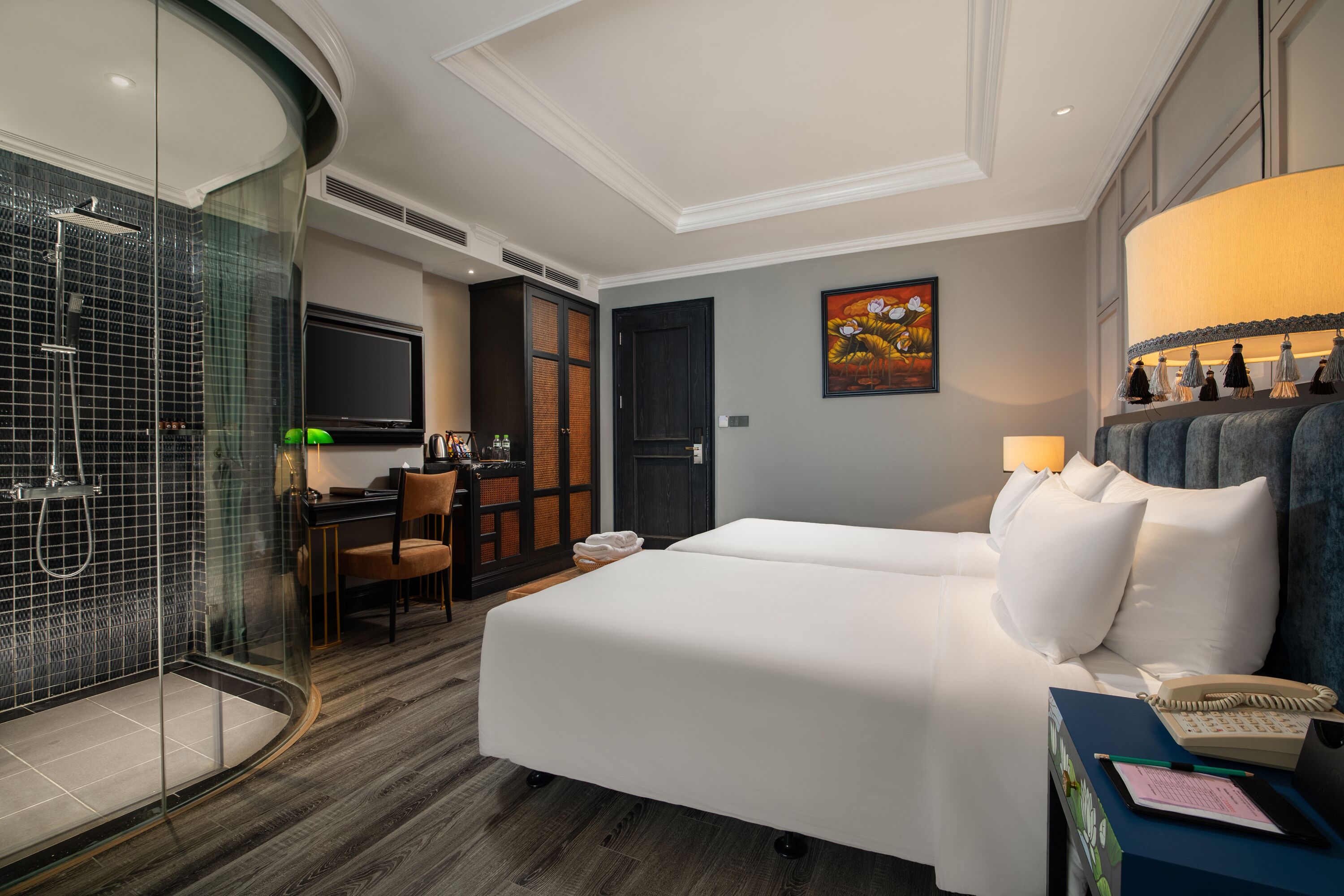 Habitación de hotel con cama, escritorio, silla, televisor, ducha y un cuadro en la pared.