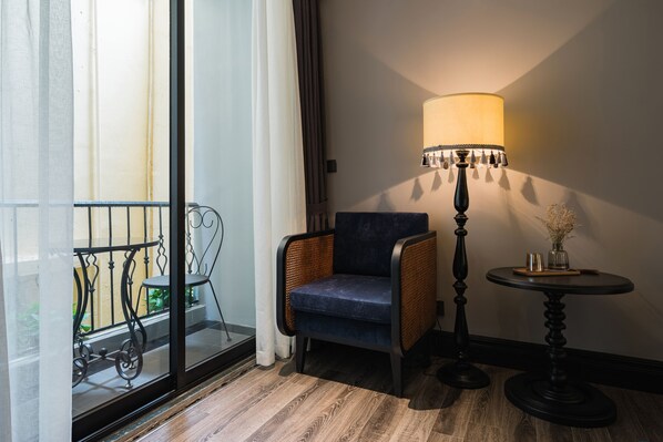 Una habitación con una silla de mimbre, una mesa con lámpara y vistas a través de un ventanal.