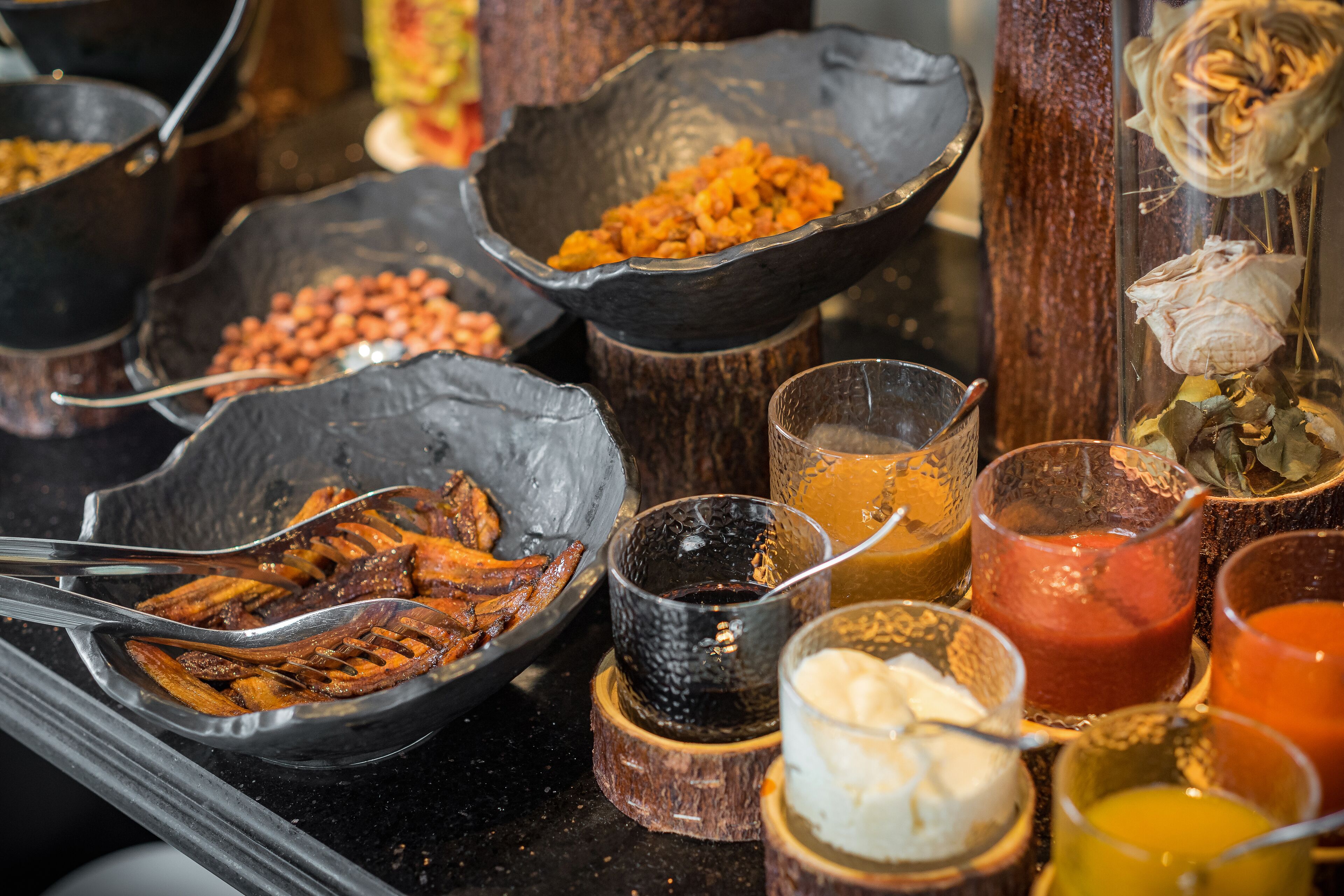 Diverse soorten eten en toevoegingen gepresenteerd in zwarte kommen en glazen op een houten oppervlak.