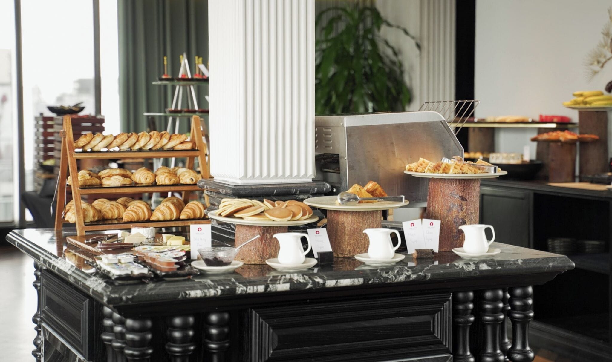A breakfast buffet with pastries, waffles, and coffee.