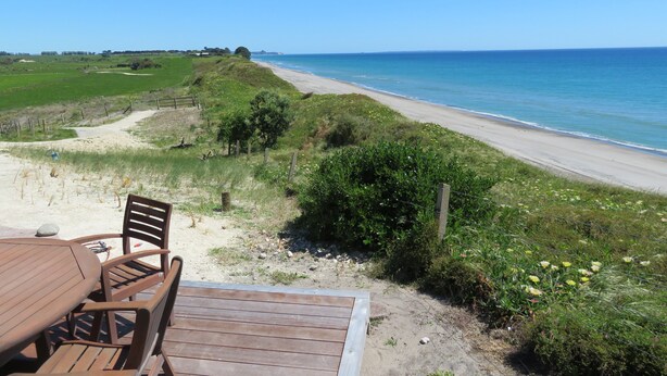 Une terrasse en bois avec des chaises, donnant sur une plage et l’océan.