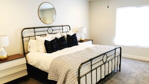 Een keurig opgemaakt slaapkamer met een metalen bed, witte beddengoed en een ronde spiegel aan de muur.