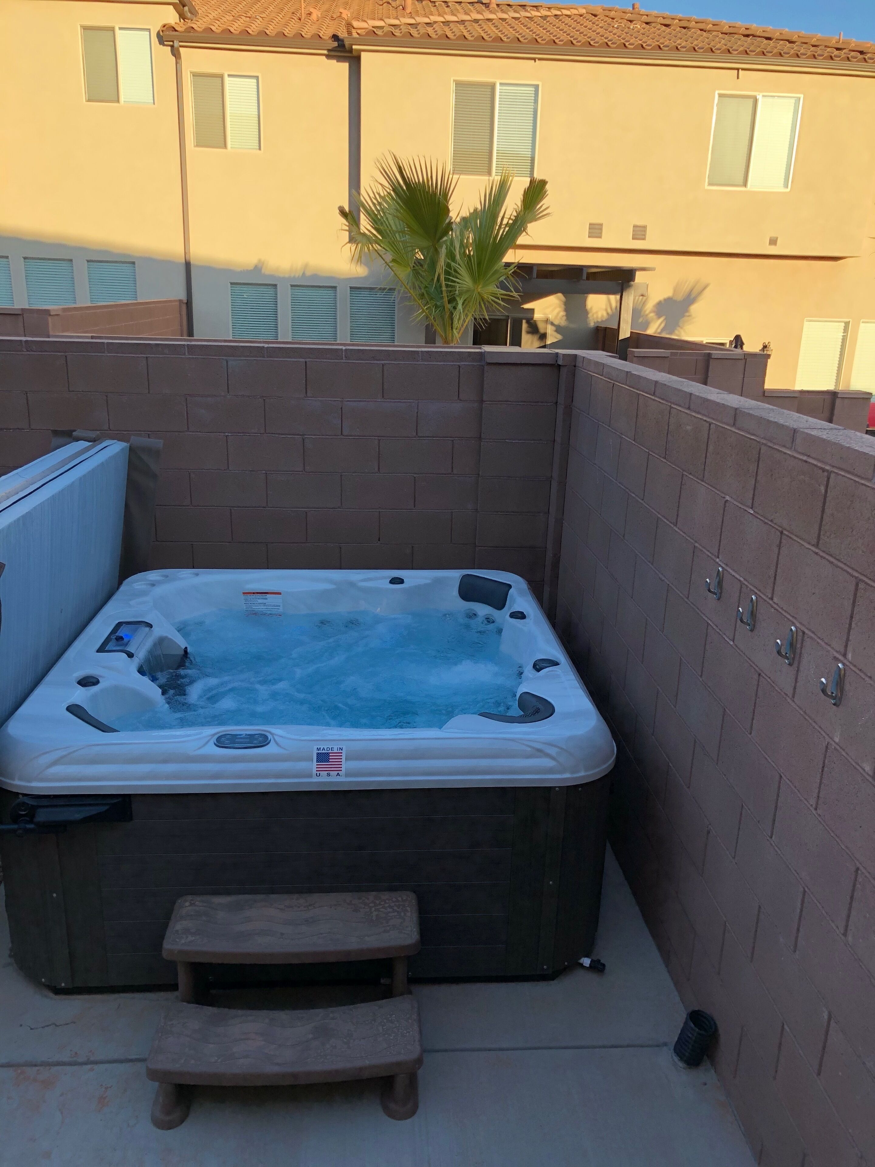 A hot tub in a corner with a wooden bench, surrounded by a brick wall.