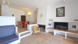 Ein Wohnzimmer mit einer Couch, einem Esstisch mit Stühlen, einem Kamin und einem Fernseher.