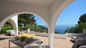 Eine Terrasse im Freien mit Esstisch, weißer Möbel und Blick auf das Meer.