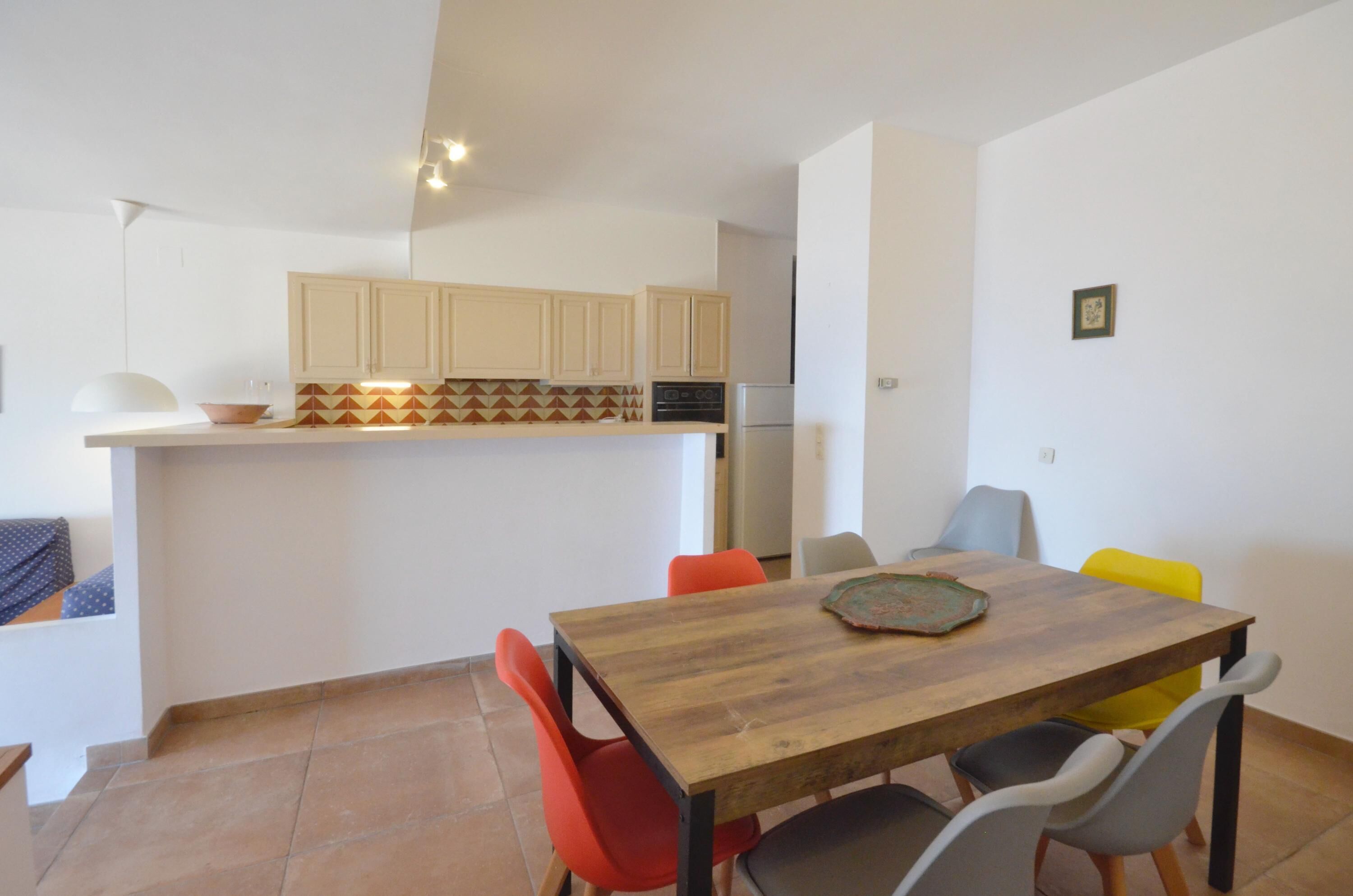 A compact kitchen with a central island, a dining table with chairs, and a small refrigerator.