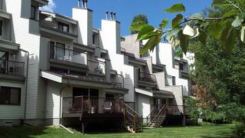 Un immeuble résidentiel à plusieurs étages, doté de balcons et d’un petit jardin devant.