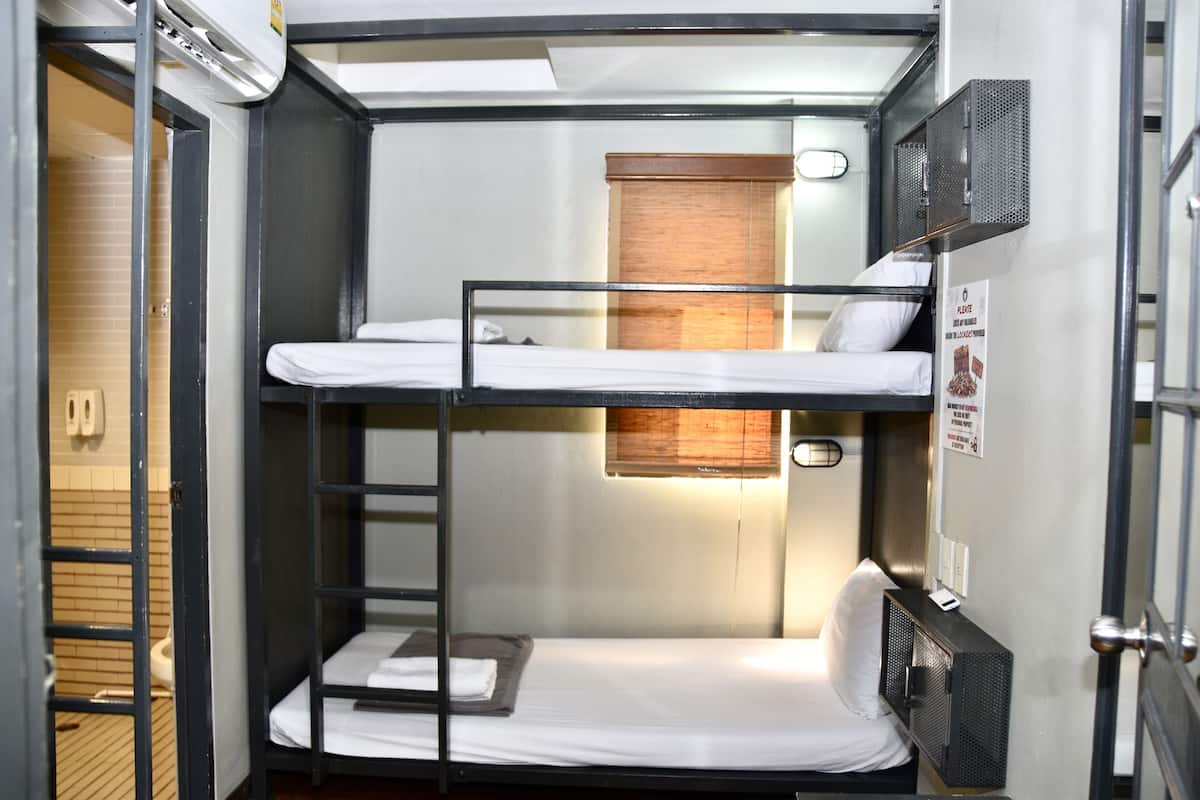 Een slaapkamer met een stapelbed, een raam, een deur en een klein plankje.