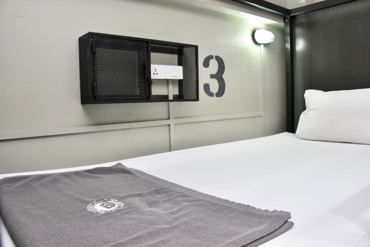 Een hotelkamer met een bed, een grijze plaid, een wandlamp en een bord met het nummer 3.