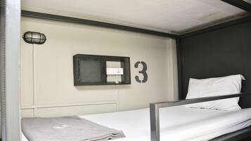 A bunk bed with a white mattress and a gray blanket. A small black-framed window is visible on the wall above the bed.