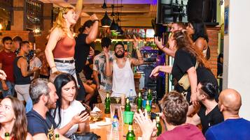 Een drukke bar met mensen die socialiseren, een barman en verschillende flessen op de toonbank.