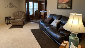 A living room with a leather sofa, a chair, a lamp, and a dining area in the background.