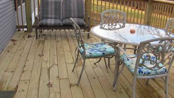 A wooden deck with a round table and chairs, a cushioned bench, and a railing.