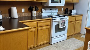 A kitchen with wooden cabinets, a white stove, a microwave, and a refrigerator.