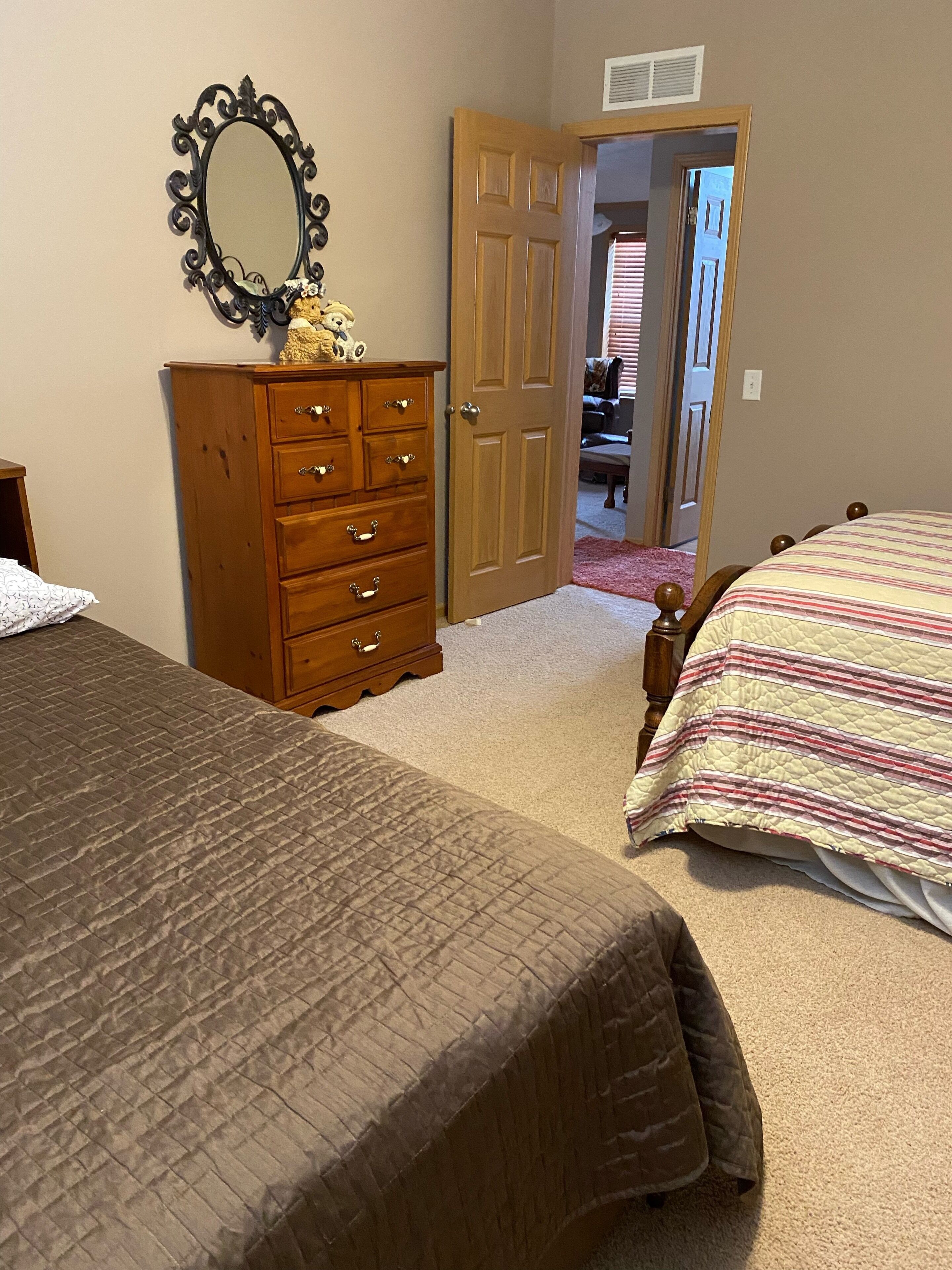 A bedroom with two beds, a wooden dresser, a mirror, and a door leading to another room.