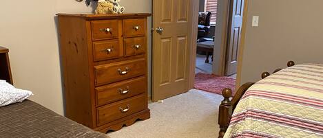 A bedroom with two beds, a wooden dresser, a mirror, and a door leading to another room.