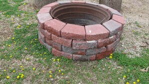 A circular fire pit made of stacked bricks with a bench in the background.