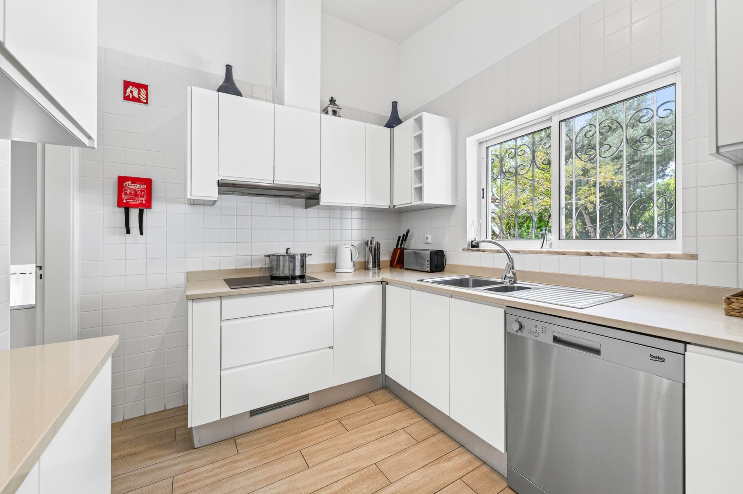 Cozinha moderna com armários brancos, máquina de lavar louça embutida e janela com vista para o verde.