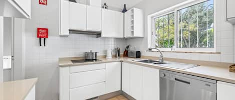 Cozinha moderna com armários brancos, máquina de lavar louça embutida e janela com vista para o verde.