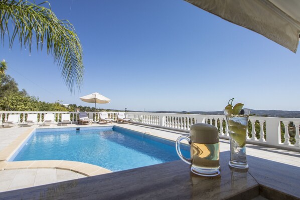 A poolside area with a clear view of the pool, lounge chairs, and a table with drinks.