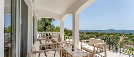 A covered outdoor seating area with tables and chairs, overlooking a scenic landscape.