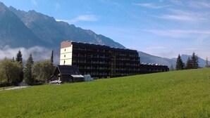 A multi-story building with a flat roof, surrounded by a grassy field and mountains in the background. - Studio with a view to the Tauplitzalm (Bad Mitterndorf)