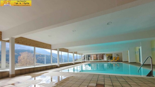 A large indoor swimming pool with a tiled floor, large windows offering a view of the mountains, and a yellow chair by the pool. - Studio with a view to the Tauplitzalm (Bad Mitterndorf)