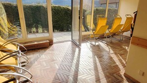 A room with yellow chairs and a herringbone-patterned floor, large windows, and a view of greenery outside. - Studio with a view to the Tauplitzalm (Bad Mitterndorf)