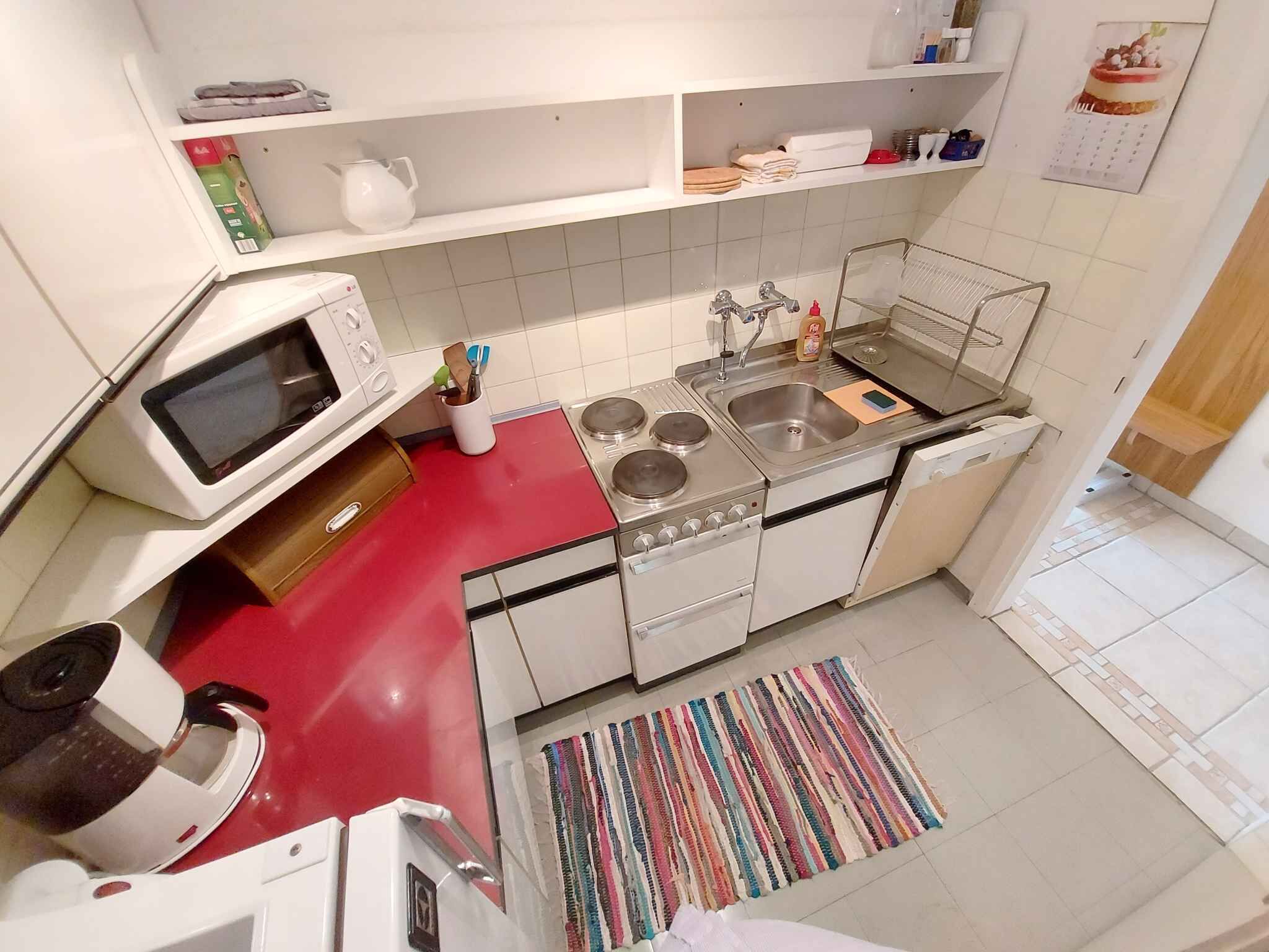 A compact kitchen with a microwave, stove, sink, and a small refrigerator.