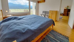 A bedroom with a bed, a desk, and a wardrobe. There is a window with a view of mountains and a chair. - Holiday apartment in the resort Sonnenalm (Sonnenalm)