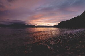 A calm lake at sunset with a rocky shoreline and distant mountains. - Sakura Beach Garden (Hiji)