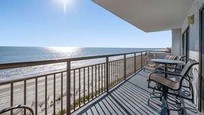 Un balcon avec vue sur la plage et l’océan, aménagé avec une table et des chaises.