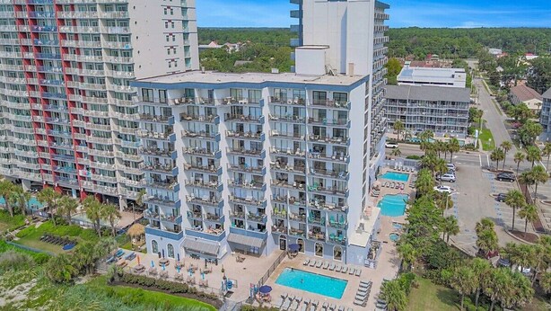 Un hôtel à plusieurs étages doté de balcons, d’une piscine et d’un espace paysager agrémenté de palmiers.