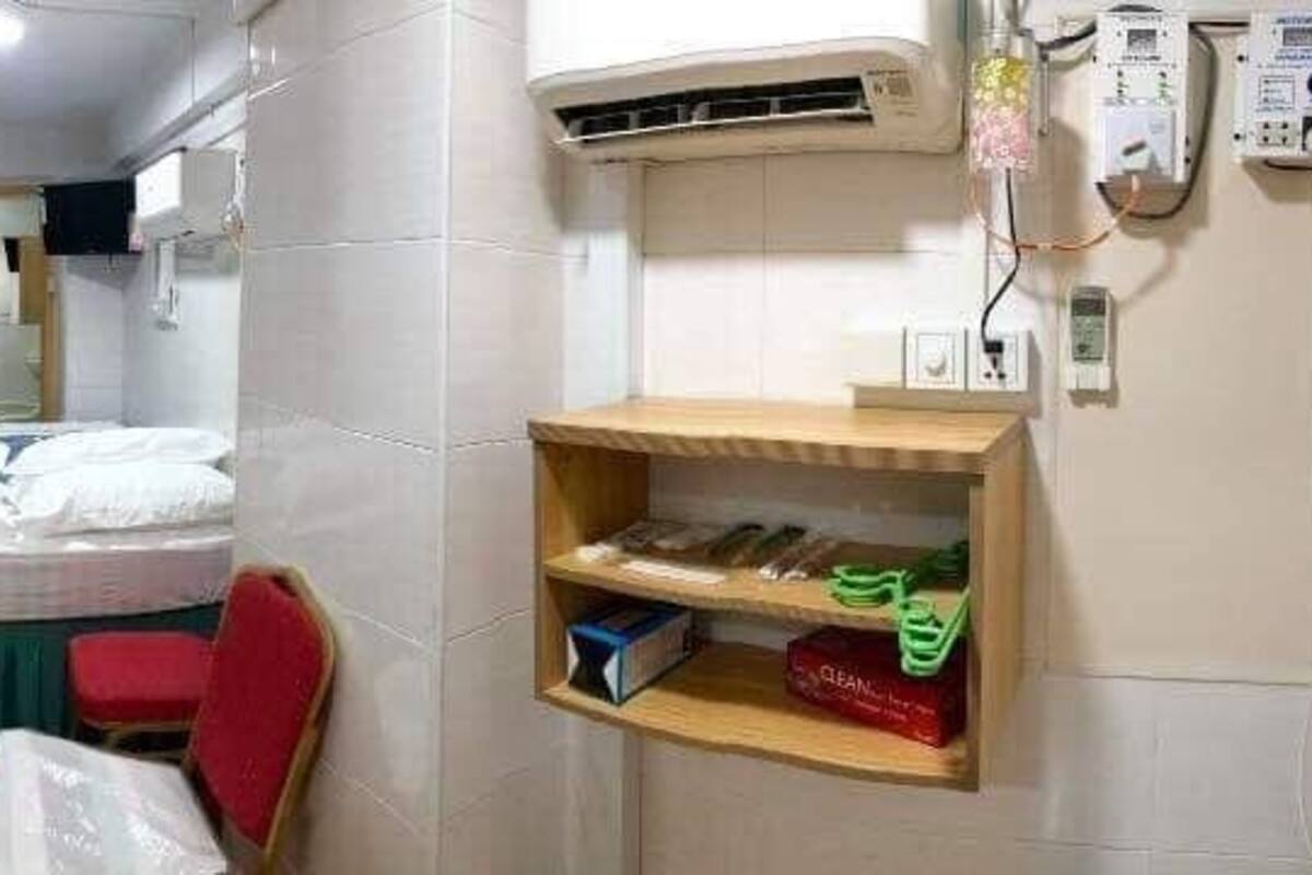 Une chambre d’hôtel de taille réduite, comprenant un lit, un petit bureau, une chaise et une étagère avec des articles de toilette.