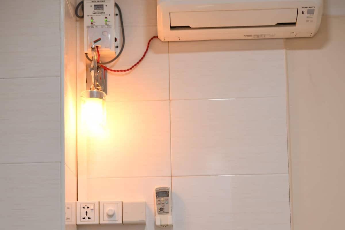 Une chambre d’hôtel avec deux lits, une table de chevet agrémentée d’une plante, un climatiseur et un téléphone fixé au mur.