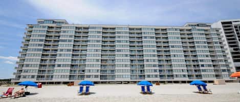 Un hôtel de grande hauteur doté de nombreux balcons et d’une plage de sable avec des parasols bleus.