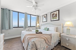 A bedroom with a bed, a nightstand, a lamp, a ceiling fan, and a window with curtains. - Sands Beach Club II 327, Lovely 2 BR Ocean Front Condo with Indoor Outdoor Swimming Pool, Hot Tub and Kiddie Pool (MYRTLE BEACH)