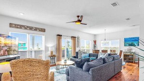 Ein geräumiges Wohnzimmer mit grauem Sofa, Korbsessel und Deckenventilator.