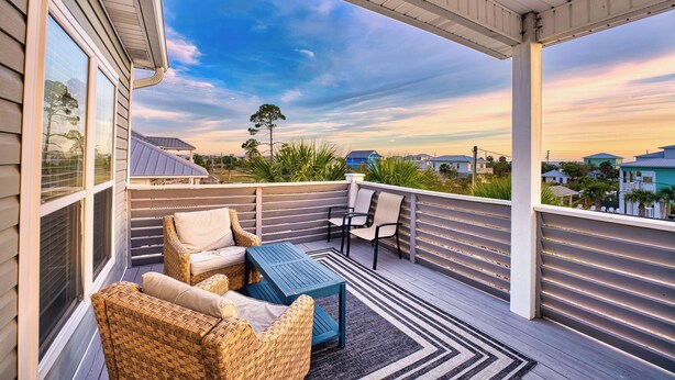 Eine überdachte Terrasse im Freien mit Korbmöbeln, einem Tisch und Blick auf die Umgebung.