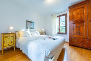 Un dormitorio con cama, armario de madera, mesitas de noche y una ventana con cortinas.