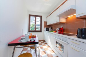 Een kleine keuken met een eettafel, stoelen, een raam en een fornuis.