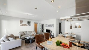 Et moderne køkken med en central ø, spiseplads og opholdsstue med sofaer og fjernsyn.
