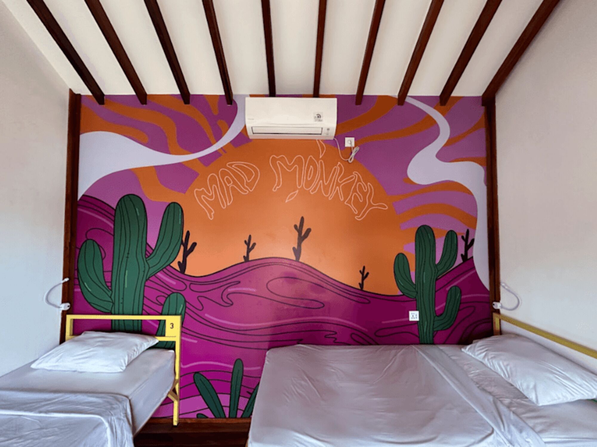 A room with two beds, a wall mural, and an air conditioning unit.