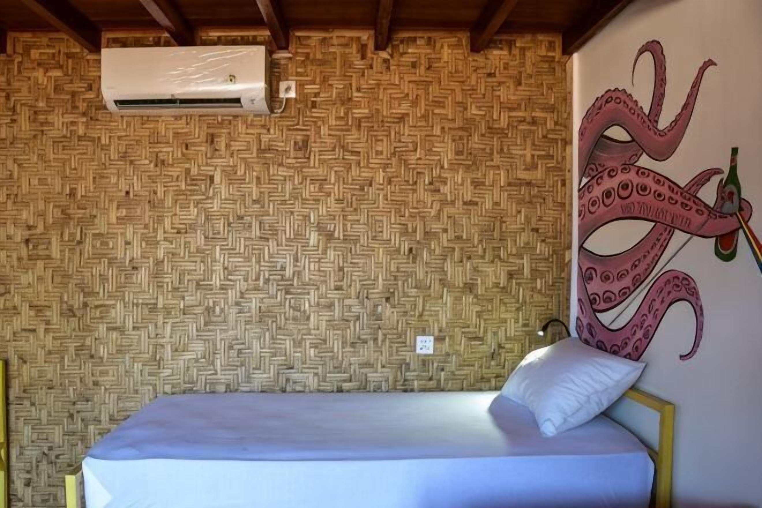 Ein Zimmer mit gewebtem Muster an der Wand, einem Bett mit weißer Matratze und einem Kissen sowie einer Wandmalerei eines Oktopus.