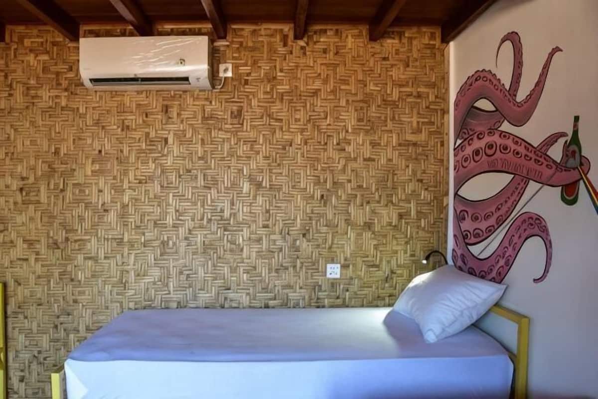 Ein Zimmer mit gewebtem Muster an der Wand, einem Bett mit weißer Matratze und einem Kissen sowie einer Wandmalerei eines Oktopus.