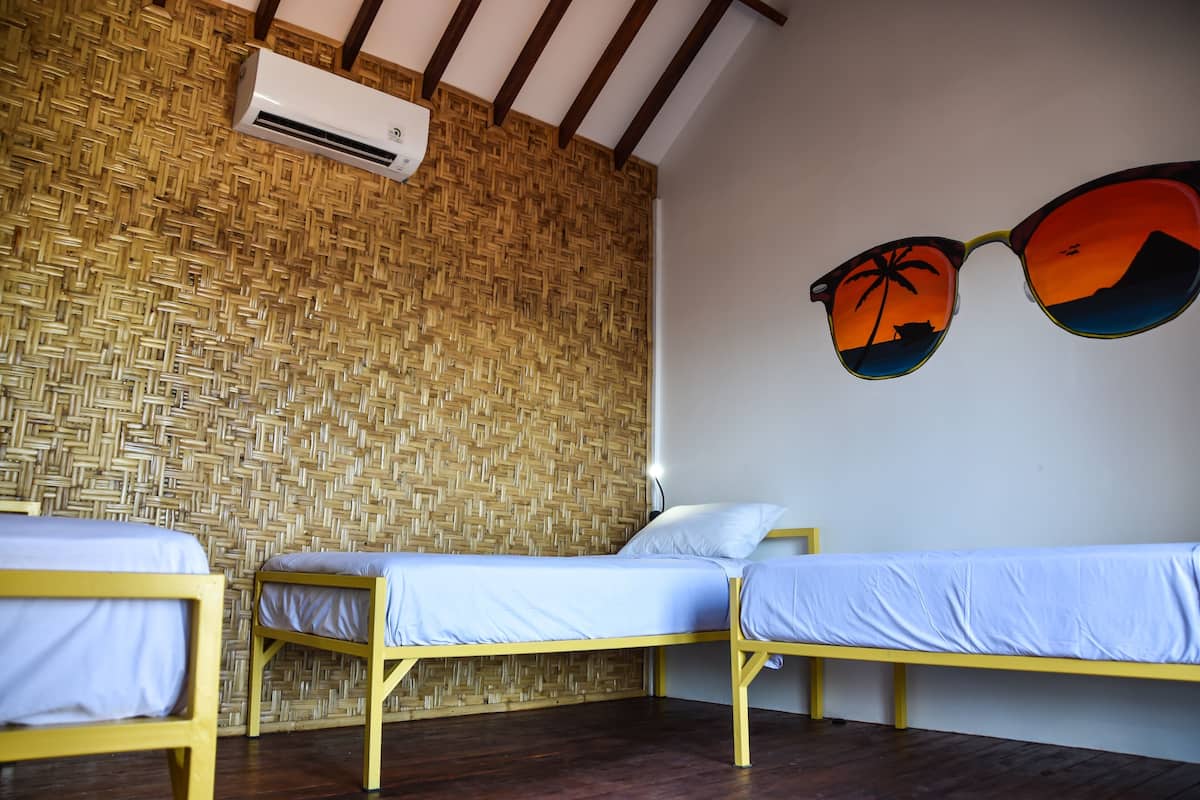 Ein Zimmer mit zwei Einzelbetten, einer gewebten Wand und einer Klimaanlage.
