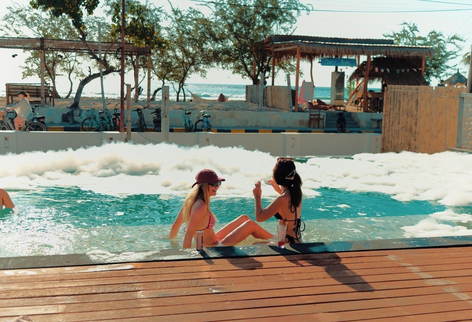A pool area with a wooden deck, a covered seating area, and a view of the sea.